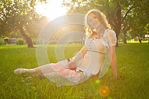 Young woman in white cute polka dot dress walking in an apple garden on a lovely sunny summer day