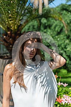 Young woman in white dress with closed eyes among tropical leaves, flowers and plants