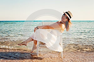 Young woman in white dress and hat sitting in a chair in the sea