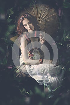 Young woman in white dress with parasol sit in fantasy garden c