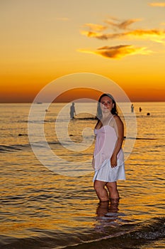 Mujer joven en blanco ropa bastidores sobre el costa sobre el atardecer 