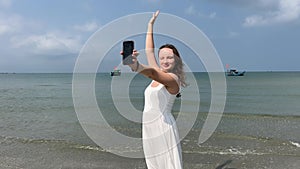 Young woman in white dress taking a selfie with mobile phone on the beach
