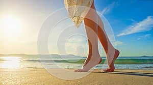 Young woman in white dress walking alone on the beach in the sun