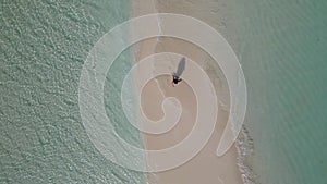 young woman in white dress walking alone on sandy beach in Maldives aeral drone view