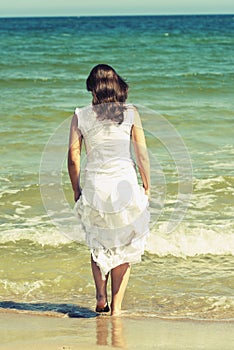 Young woman in white dress walking on the beach.