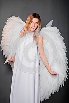 woman in a white dress with white wings behind her back. Girl in the image of an angel isolated on a gray background