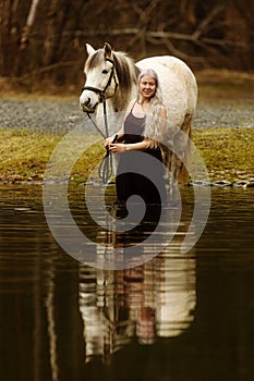 young woman with white hairis Ã­n the water with white horse