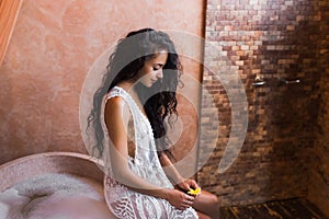Woman in white lingerie relaxing near stone bath full foam in moroccan bathroom