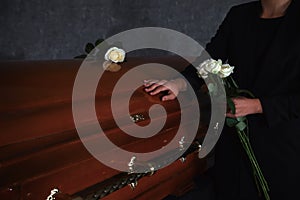 Young woman with white roses near casket in funeral home