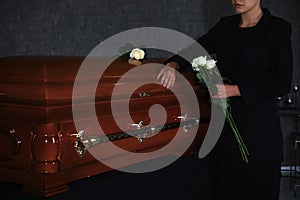 Young woman with white roses near casket in funeral home,