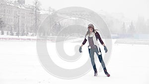 A young woman with white scarf ice skating outside. Heavy snowfall