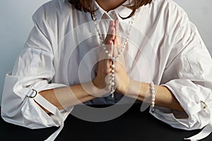 A young woman, in a white shirt folding a lodon to each other prays to God holding rosary