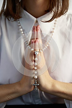 A young woman, in a white shirt folding a lodon to each other prays to God holding rosary.