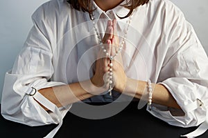 A young woman, in a white shirt folding a lodon to each other prays to God holding rosary.