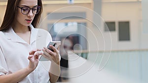 Young woman in a white shirt and glasses uses smartphone to search for information on the Internet.