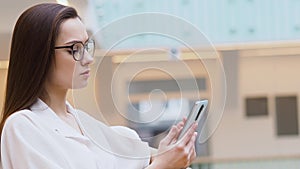 Young woman in a white shirt and glasses uses smartphone to search for information on the Internet.