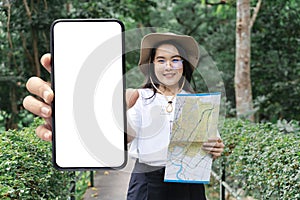 Young woman in white shirt holding big smartphone with blank white screen at forest park, road trip, transportation