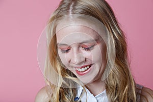 Young woman in white shirt is smiling look down, pink background