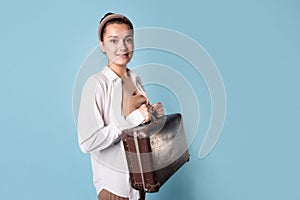 young woman in a white shirt stands grabbing her luggage. A traveler