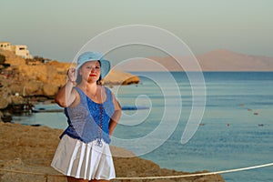 Young woman in a white skirt and a sun hat on the background of the sea at sunset.