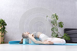 Young woman in white sportwear practicing yoga indoors at home. Exercises with yoga blocks. Home workout