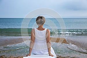 A young woman in a white sundress sits on a deck chair by the sea and enjoys a beautiful view and tranquility. Holidays on the