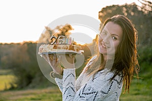 Young woman in white sweater holding a birthday cake with misplaced candles. Copy space