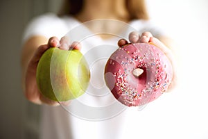 Young woman in white T-shirt choosing between green apple or junk food, donut. Healthy clean detox eating concept