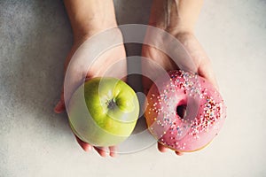 Young woman in white T-shirt choosing between green apple or junk food, donut. Healthy clean detox eating concept
