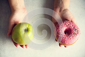 Young woman in white T-shirt choosing between green apple or junk food, donut. Healthy clean detox eating concept