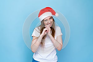 Young woman in white t-shirt with christmas hat on blue background. Cute santa