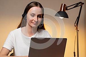 Young woman in a white T-shirt and headset is working on a laptop computer at home. Work at home, Video conference