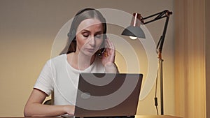 Young woman in a white T-shirt and headset is working on a laptop computer at home. Work at home, Video conference