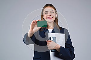 Young woman in white t-shirt holding credit card near face and laptop, isolated over gray background. Pay wit credit or