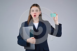 Young woman in white t-shirt holding credit card near face and laptop, isolated over gray background. Pay wit credit or