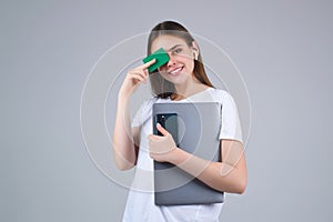 Young woman in white t-shirt holding credit card near face and laptop, isolated over gray background. Pay wit credit or