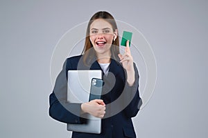 Young woman in white t-shirt holding credit card near face and laptop, isolated over gray background. Pay wit credit or