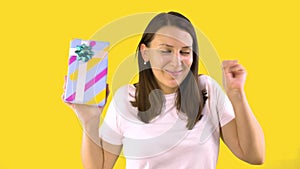 Young Woman in White T-shirt Holds Beautiful Box with a Gift and Rejoices. Back Yellow Background.