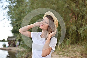 Young woman in white t-shirt holds a straw hat with her hands and looks at the blue sky sitting on the shore. girl dreaming