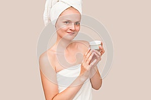 Young woman in white towel apply moisturizer cream on bright isolated background. Skin care, spa concept
