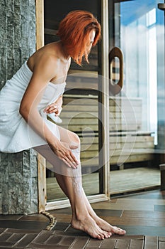 Young woman in white towel does body massage with organic natural scrab in the sauna, treat yourself photo