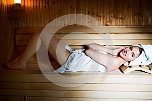 Young woman in white towel lying in Finnish sauna