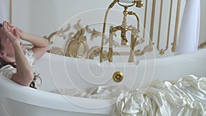 Young woman in white wedding dress lying in the amazing ampty bath, girl remove her hat with flowers and throwing in the