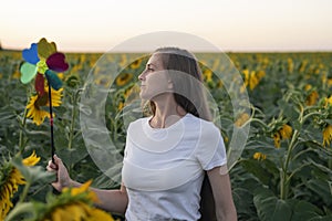 Young woman with windmill toy walks through the sunflower field. Alternative energy. Green energy concept