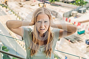 A young woman by the window annoyed by the building works outside. Noise concept