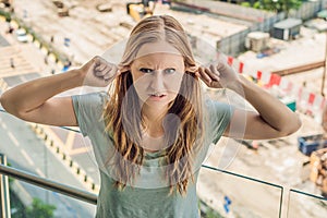 A young woman by the window annoyed by the building works outside. Noise concept