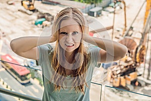 A young woman by the window annoyed by the building works outside. Noise concept