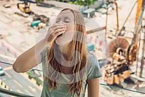 A young woman by the window annoyed by the building works outside. Noise concept