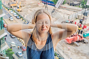 A young woman by the window annoyed by the building works outside. Noise concept