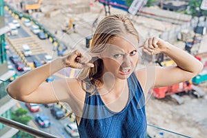 A young woman by the window annoyed by the building works outside. Noise concept